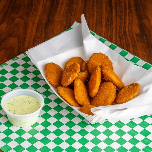 Golden-brown fried zucchini bites in a paper tray with a side of creamy green dipping sauce.