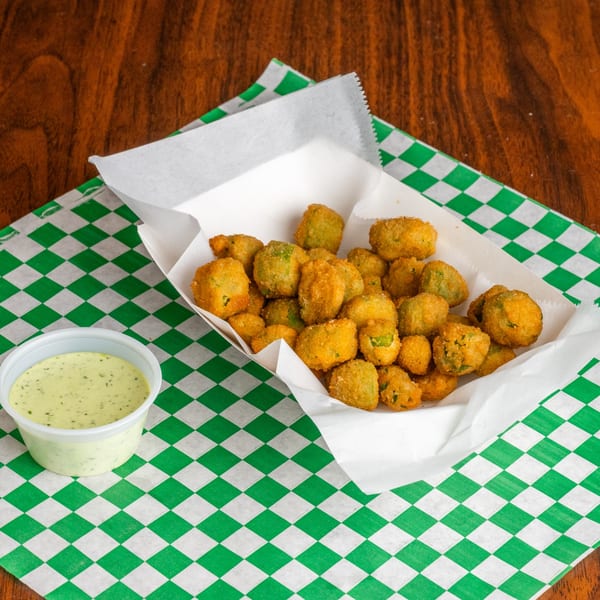 Fried okra in a paper tray with a side of creamy green dipping sauce on a checkered liner.