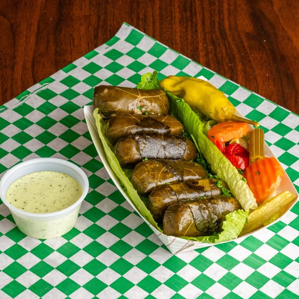 Dolmades, or stuffed grape leaves, with pickled vegetables and a side of creamy sauce on a checkered paper.