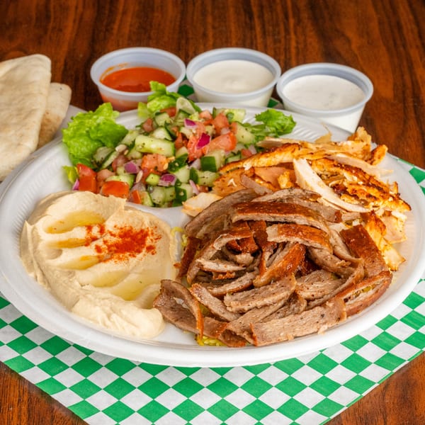A Mediterranean platter with hummus, salad, pita bread, and two types of shawarma meat.