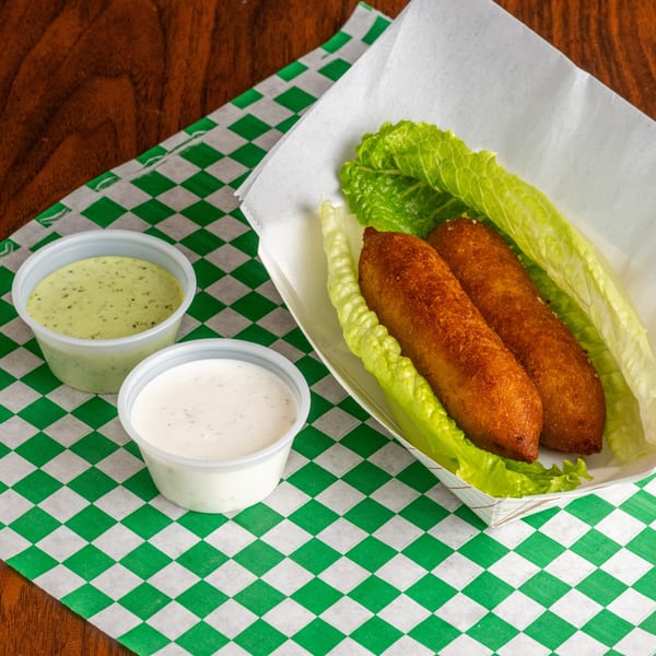 Two fried kibbeh on lettuce in a paper tray, with two dipping sauces on a checkered green and white paper.