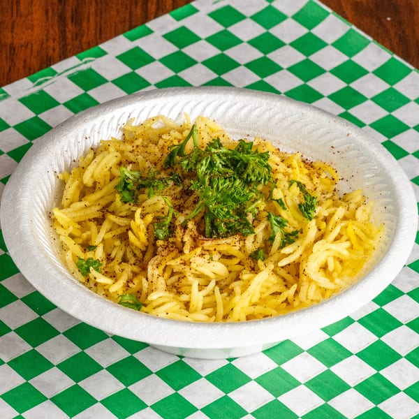 A white bowl of yellow rice, seasoned with pepper and garnished with fresh parsley, on a green and white checkered paper.
