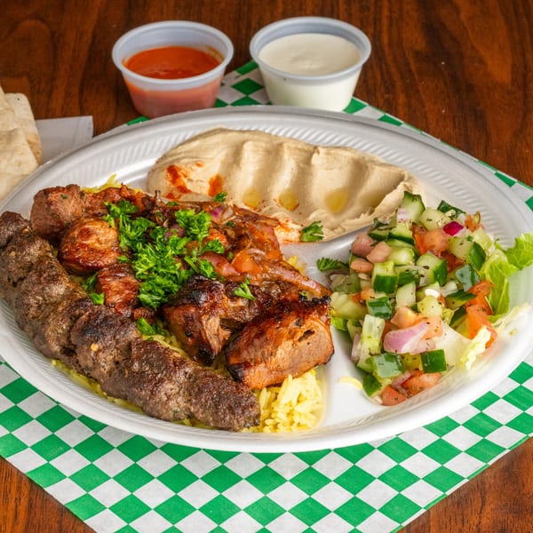 A Mediterranean platter with grilled meats, rice, hummus, and a fresh cucumber tomato salad.